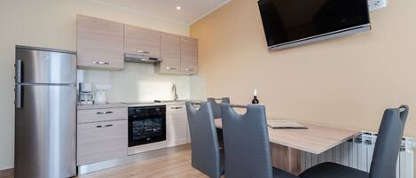 A modern kitchen with stainless steel appliances, a dining area with a table and chairs, and a mounted TV on the wall.