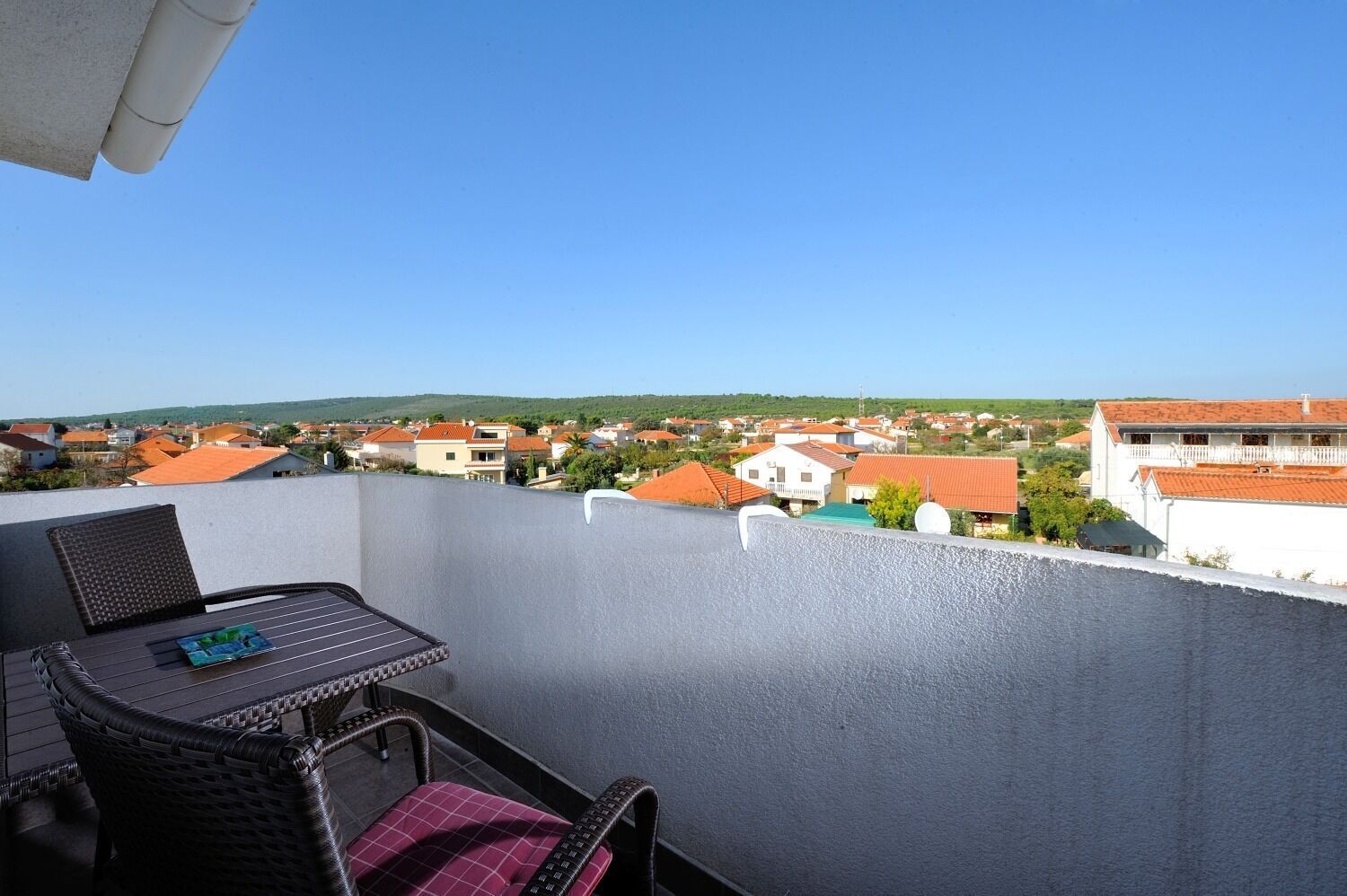 A balcony with a table and chairs, overlooking a residential area with houses and a clear sky.