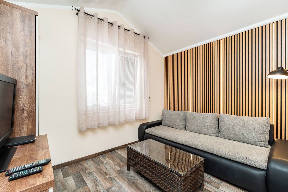 A living room with a sofa, a television, a coffee table, and a curtain.