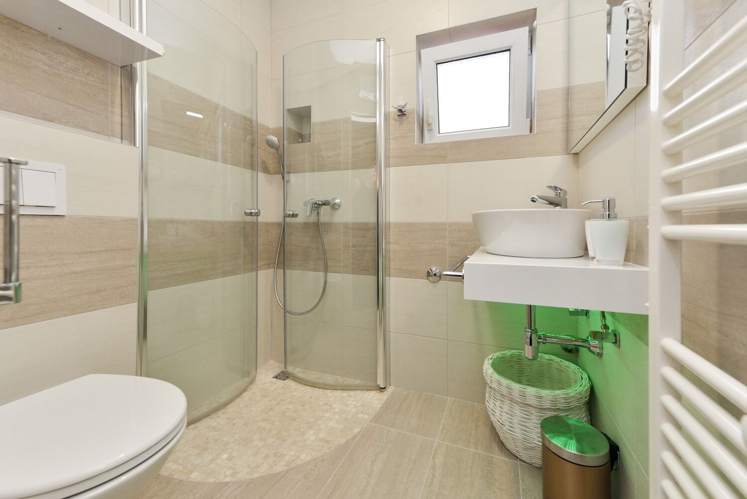 A modern bathroom with a glass-enclosed shower, a toilet, a sink with a mirror, and a small window.