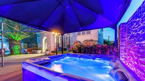 A hot tub under a blue canopy with a stone wall and flowers in the background.