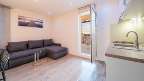 A modern living room with a grey sectional sofa, a small round coffee table, and a glass door leading to a balcony with a city view.
