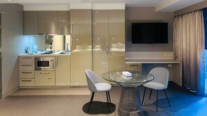 A modern hotel room with a kitchenette, a flat-screen TV, and two checkered chairs around a glass table. - Minton Apartments (Melbourne)