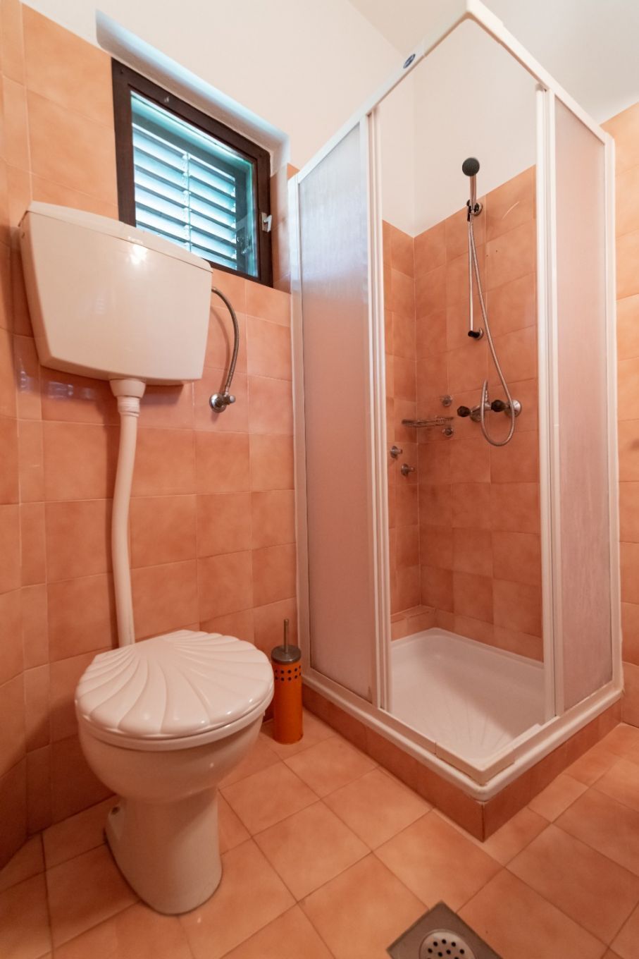 A bathroom with a toilet, a shower enclosure, and a window with blinds.