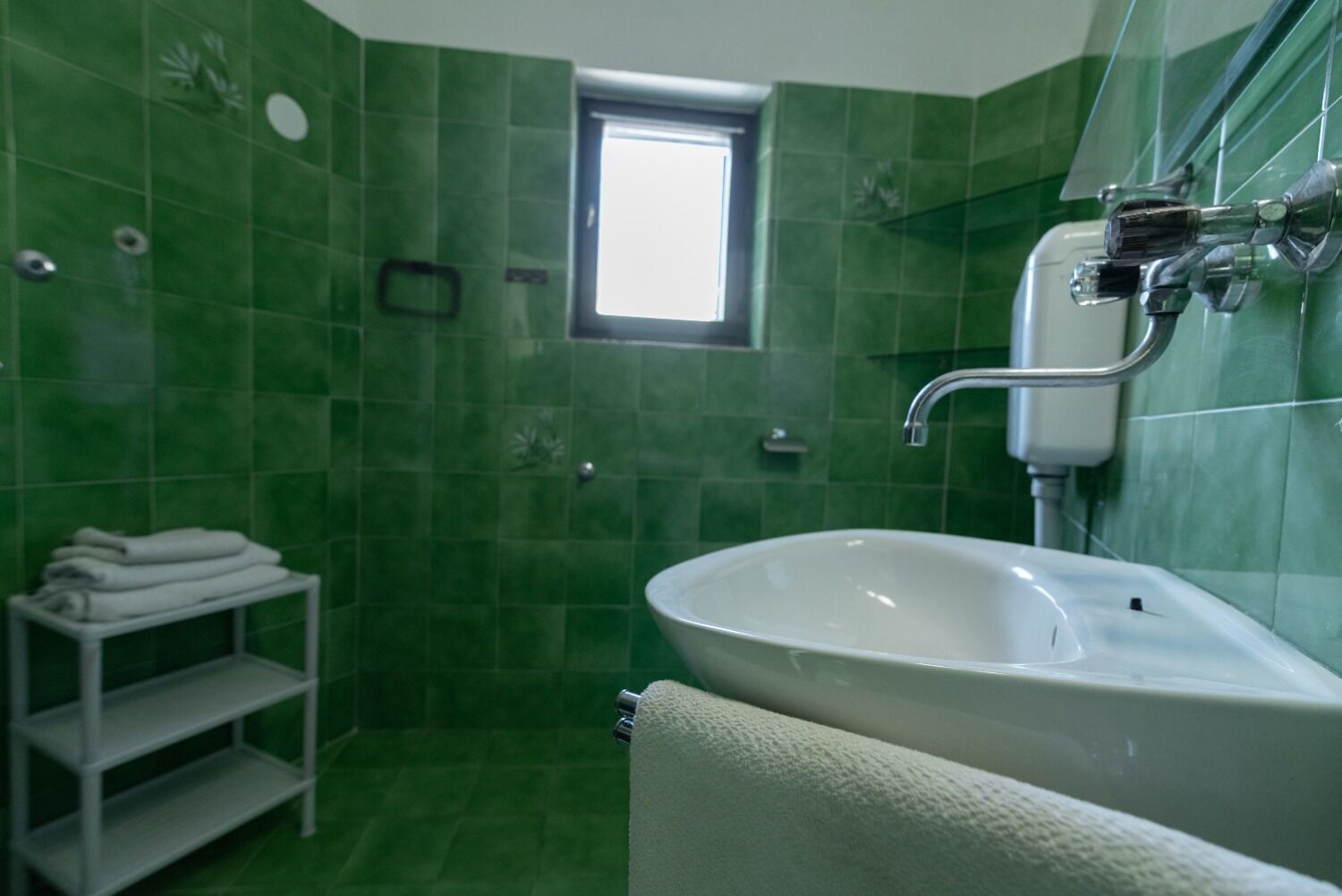 Une salle de bain avec des carreaux verts, un lavabo blanc, une fenêtre et un porte-serviettes.