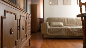 Ein hölzerner Schminktisch mit mehreren Schubladen und einer Tür, ein gestreiftes Sofa und ein Holzstuhl in einem Zimmer mit Holzboden.