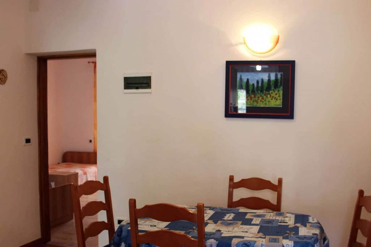 A small dining area with a table and chairs, a wall-mounted picture, a ceiling light, and a fan.