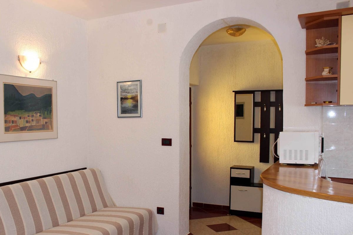 A cozy room with a striped sofa, a painting, and a small kitchen area with a refrigerator and a microwave.