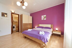A bedroom with a bed, wooden floor, a washing machine, and a nightstand with a lamp. - Apartment and Rooms Ivo (Trogir)