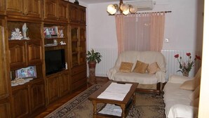 A living room with a wooden cabinet, a television, a beige sofa, and a patterned rug. - Apartments Mirko (Tkon)