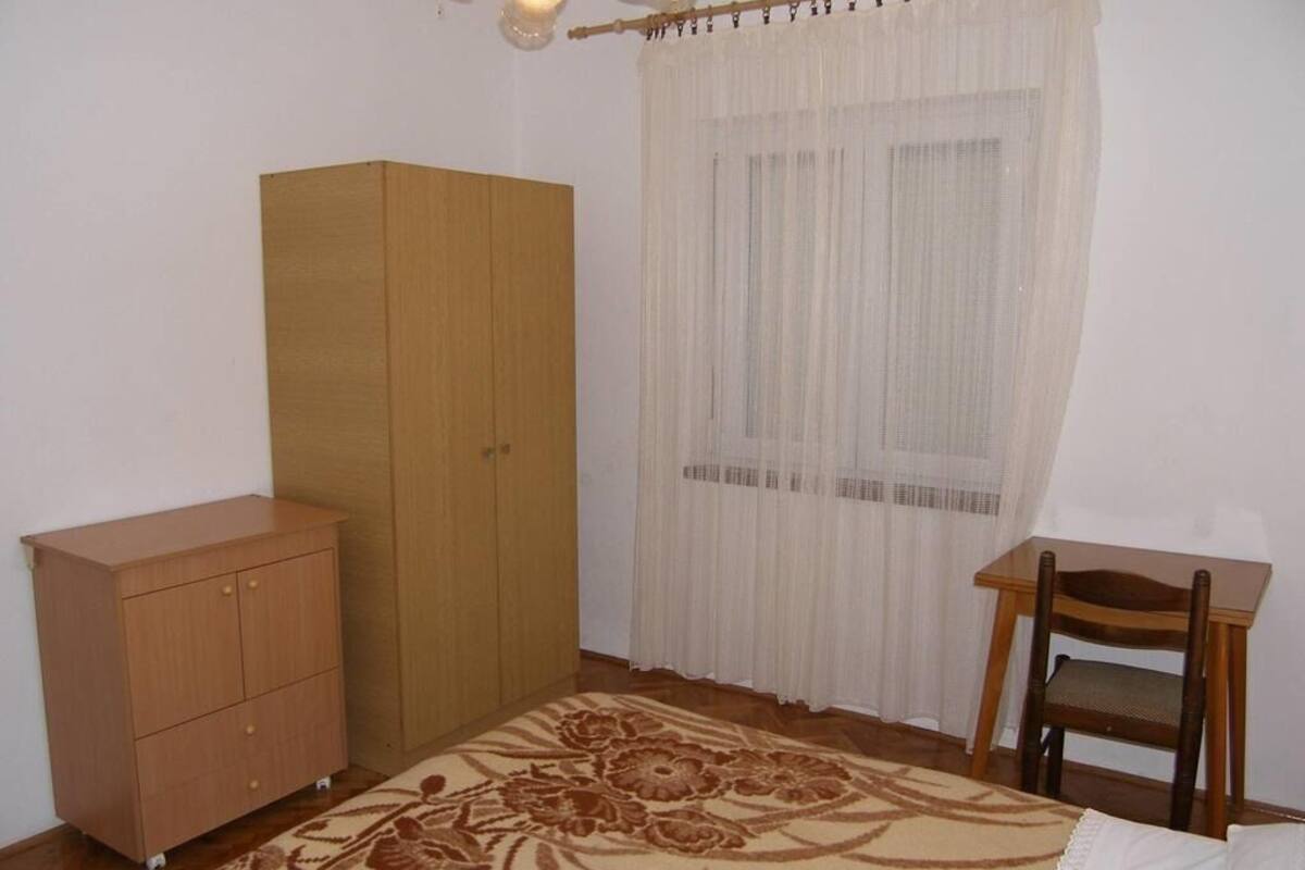 A bedroom with a wardrobe, a chair, a bed, and a window with curtains.