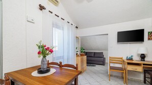 Zona pranzo con tavolo in legno, sedie, un vaso con fiori, un divano, una televisione e una lampada.