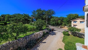 Una strada di campagna fiancheggiata da muri in pietra e vegetazione, che conduce a un edificio con tetto in tegole.