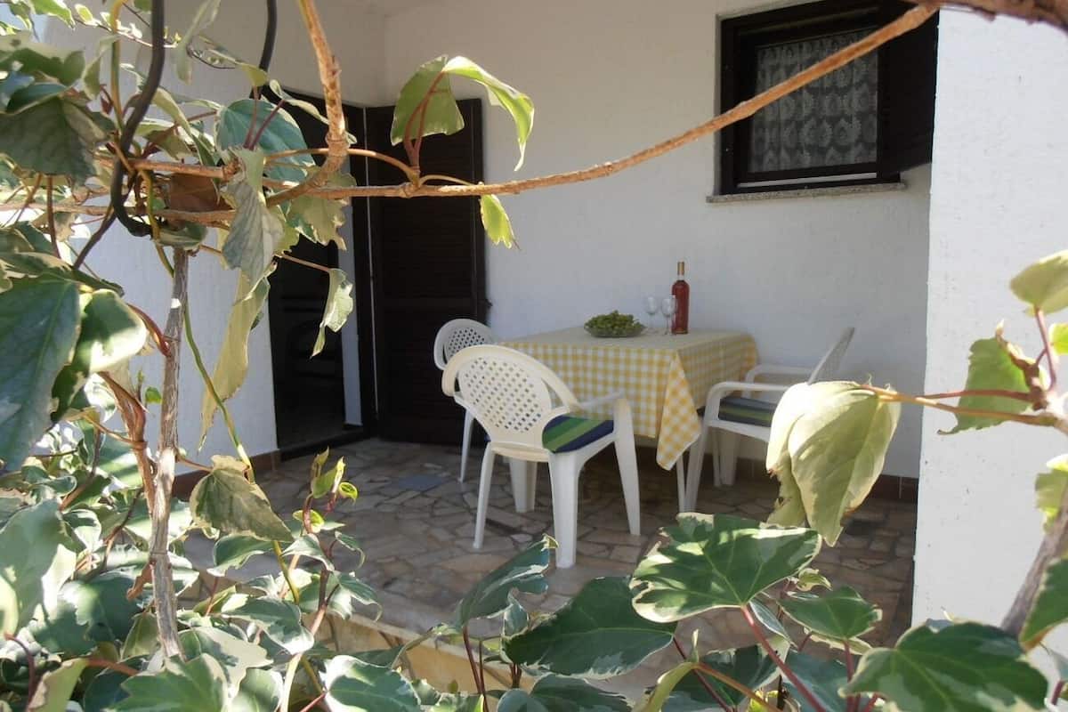 Un patio exterior con una mesa y sillas, una ventana con persiana decorativa y una puerta con contraventanas oscuras.