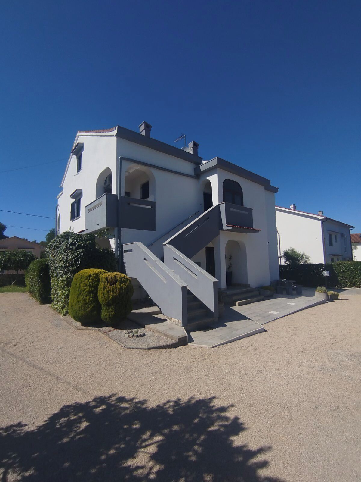 A two-story building with a staircase leading to the entrance, surrounded by neatly trimmed bushes.