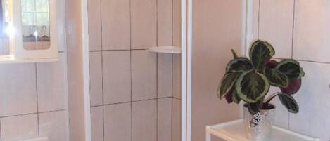 A bathroom with a shower enclosure, a sink, a mirror, and a shelf with towels and a potted plant.