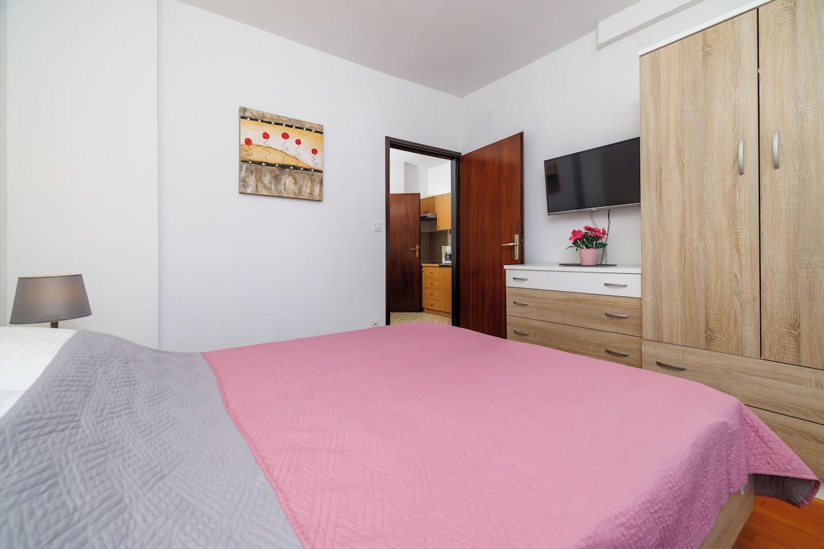 Un dormitorio con cama, televisor, armario y un cuadro en la pared.