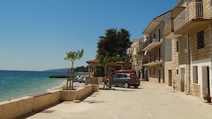 A coastal street with stone buildings, a parked car, and a clear blue sky. - Apartment Inga (Gradac)