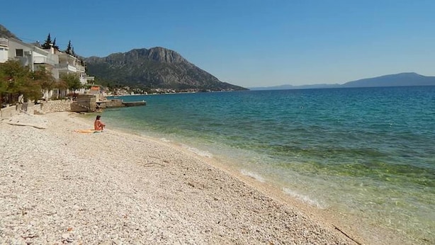 A pebbled beach with clear water, a mountain in the background, and buildings on the left. - Apartment Inga (Gradac)