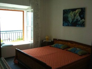 A bedroom with a bed, a window, a nightstand, and a painting. - Apartment Inga (Gradac)