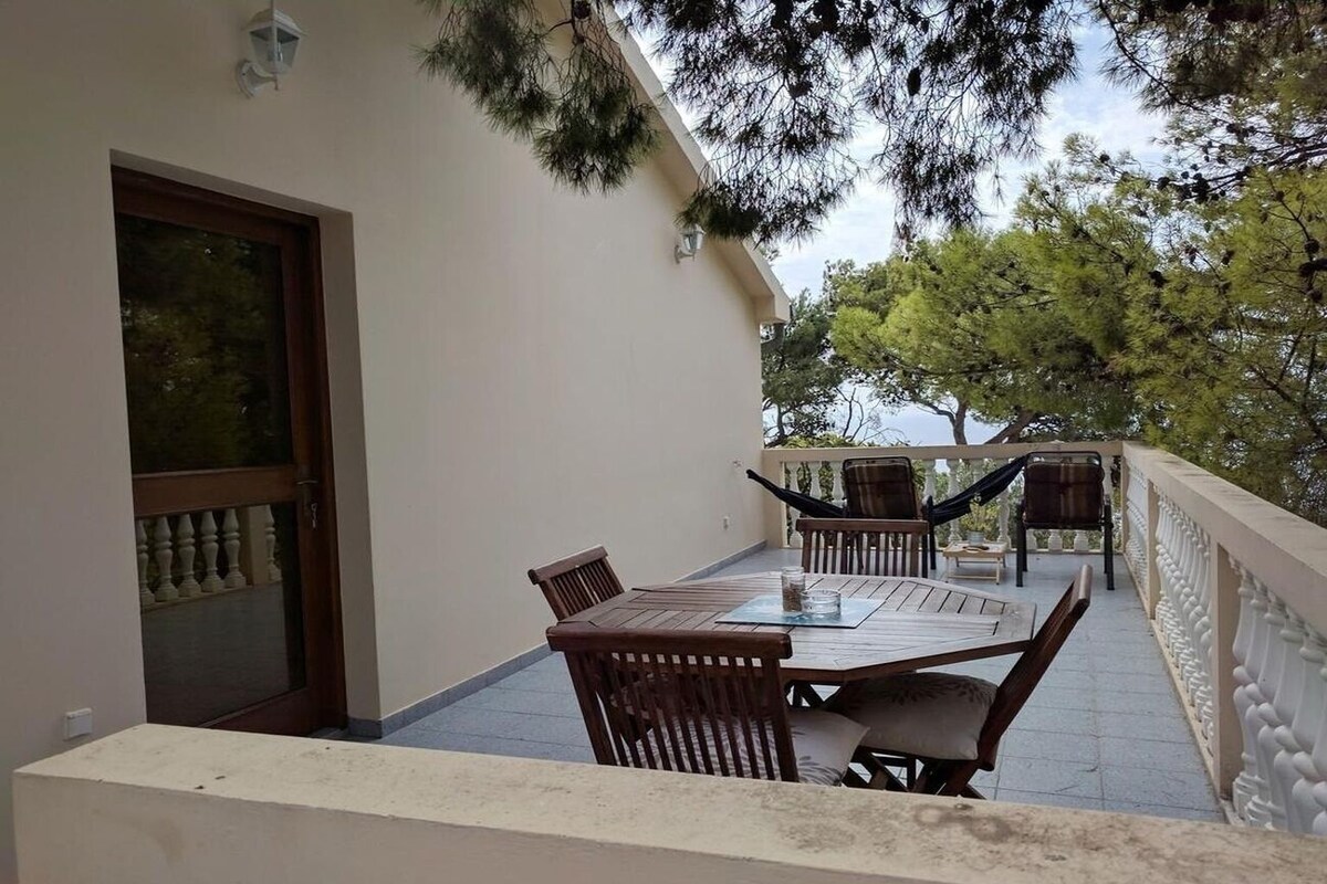 Ein Balkon mit Tisch, Stühlen, einer Tür und Blick auf Bäume.