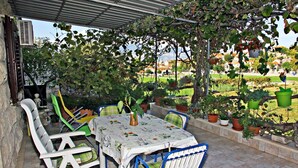 An outdoor patio with a table and chairs, surrounded by potted plants and a view of a garden and buildings in the background.