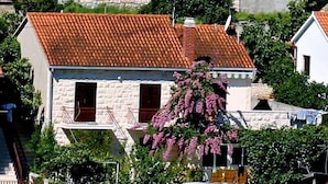 A cluster of stone buildings with red-tiled roofs, some with balconies and windows, surrounded by greenery.