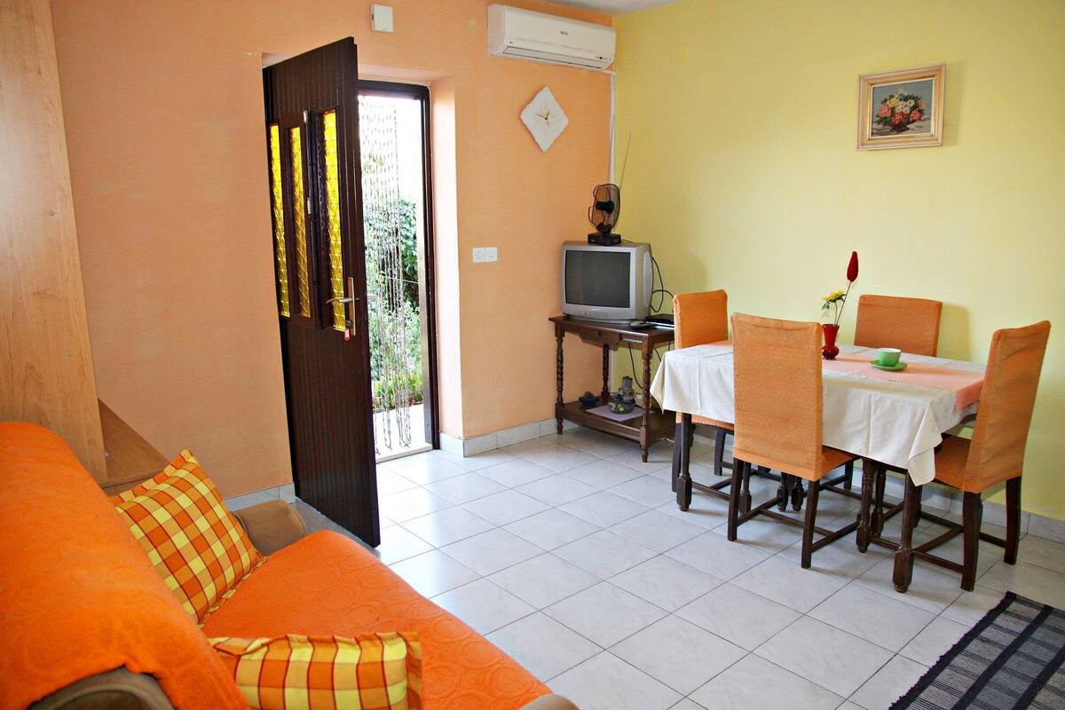 Ein Zimmer mit Sofa, Esstisch, Stühlen, Fernseher und einer Wanduhr.