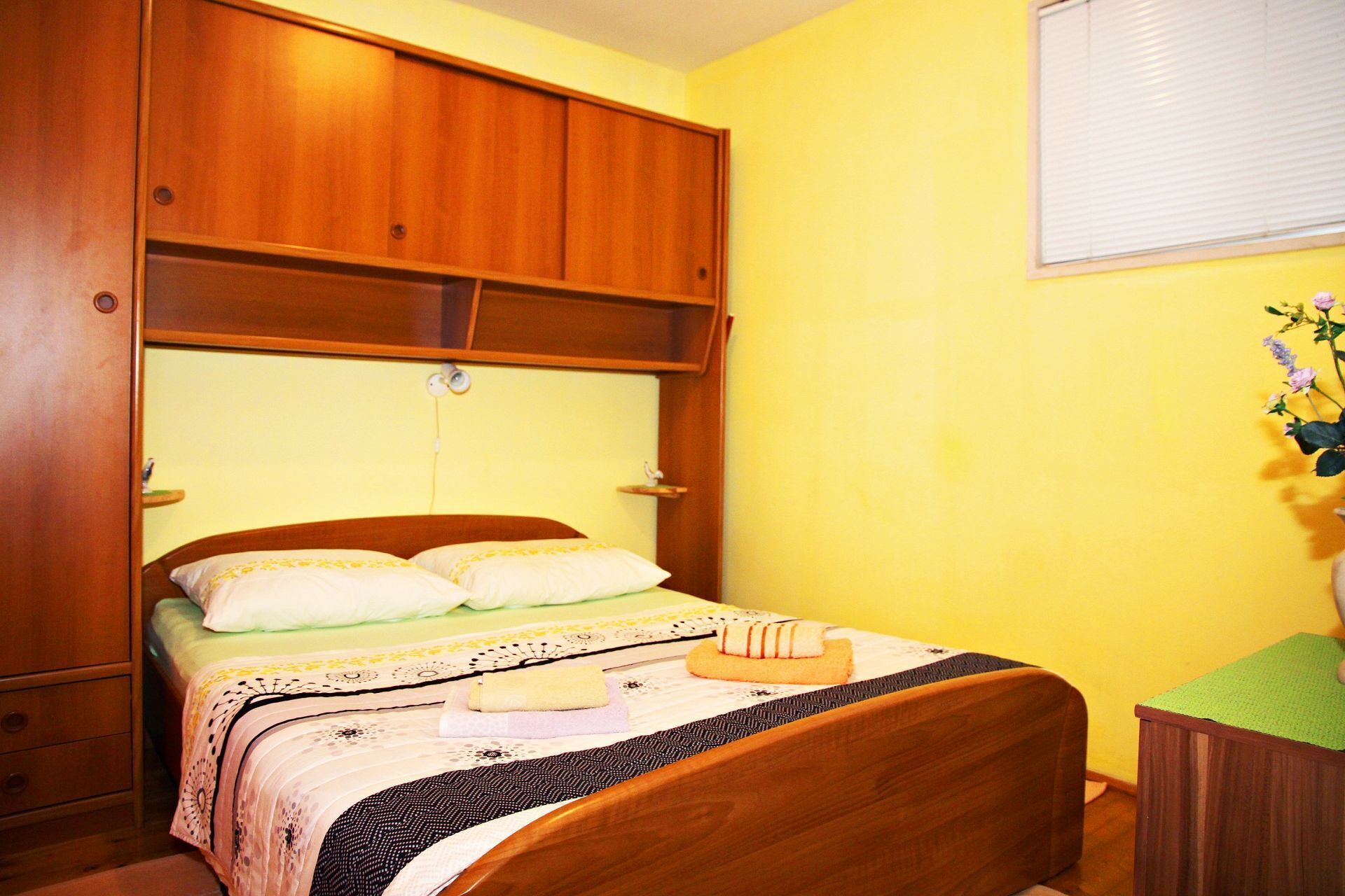 Un dormitorio con cama de madera, una mesita de noche y una ventana con persianas.