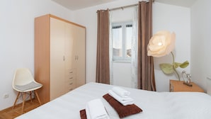 A bedroom with a bed, a wardrobe, a chair, a window with curtains, and a flower vase. - Apartments Mari (Zadar)