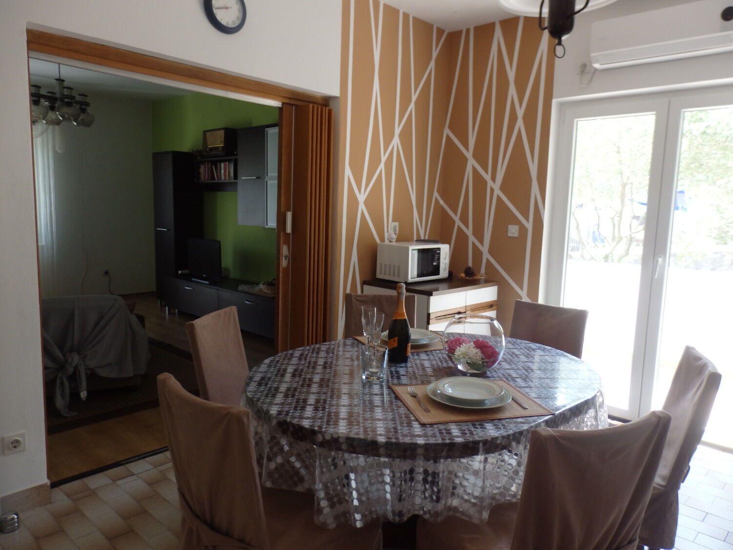 Un comedor con una mesa redonda, sillas, un reloj, un microondas y vistas al exterior.