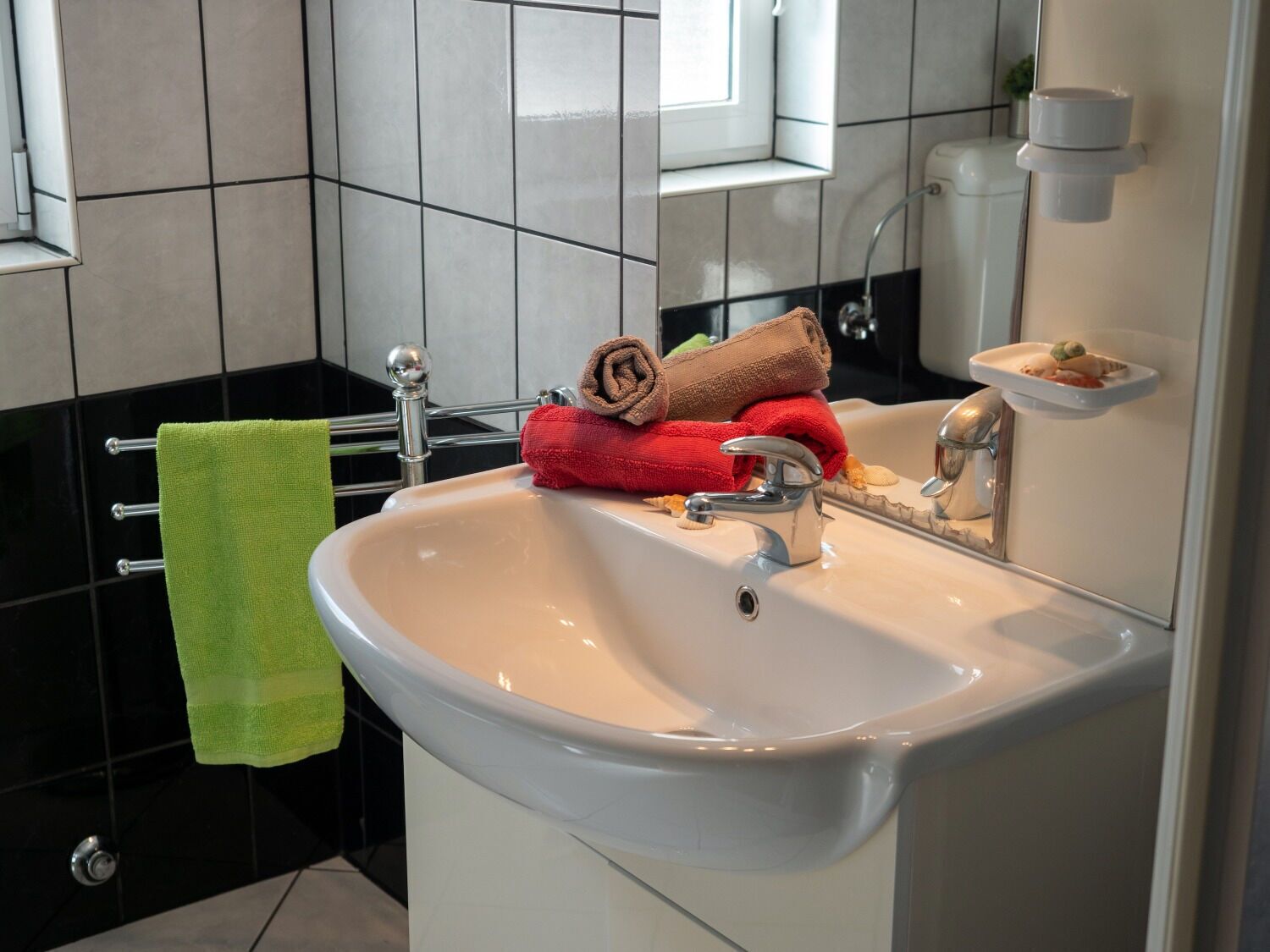 Un baño con un lavamanos blanco, un espejo y un toallero con una toalla verde.