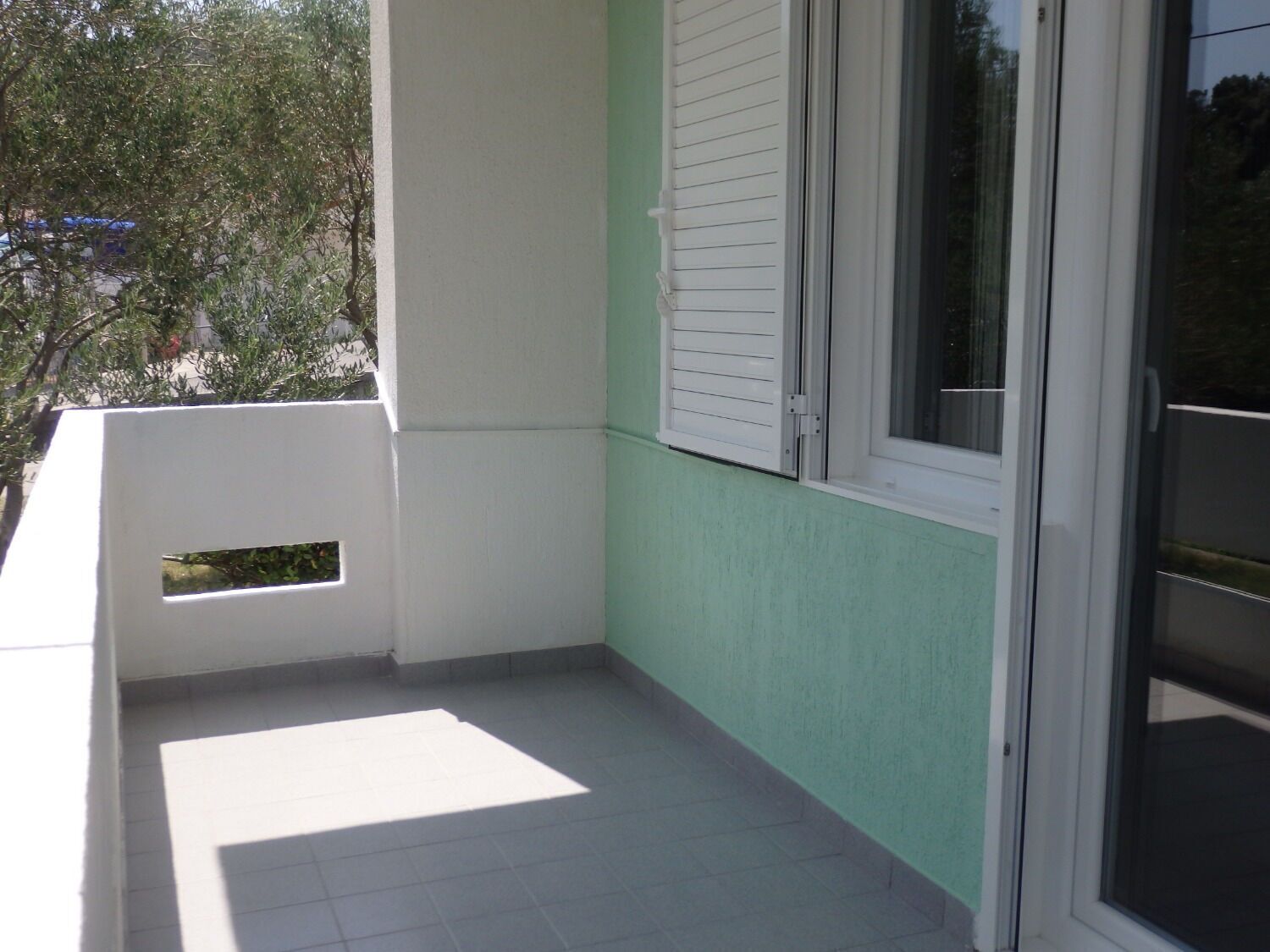 A balcony with a white railing, a window with white shutters, and a green wall.
