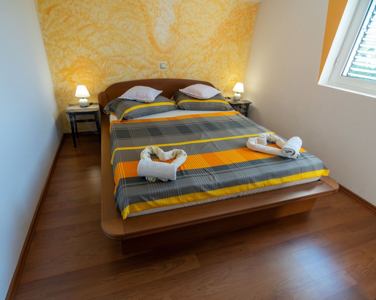 A neatly made bed with striped bedding, two bedside tables with lamps, and a window with blinds.