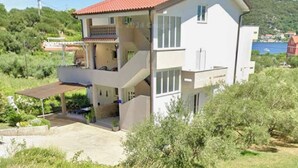 Una casa de dos pisos con techo rojo, un balcón en el nivel superior y una entrada con camino de acceso.