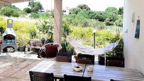 Un patio exterior con una mesa y sillas, una hamaca, una parrilla y vistas a zonas verdes y edificios al fondo.
