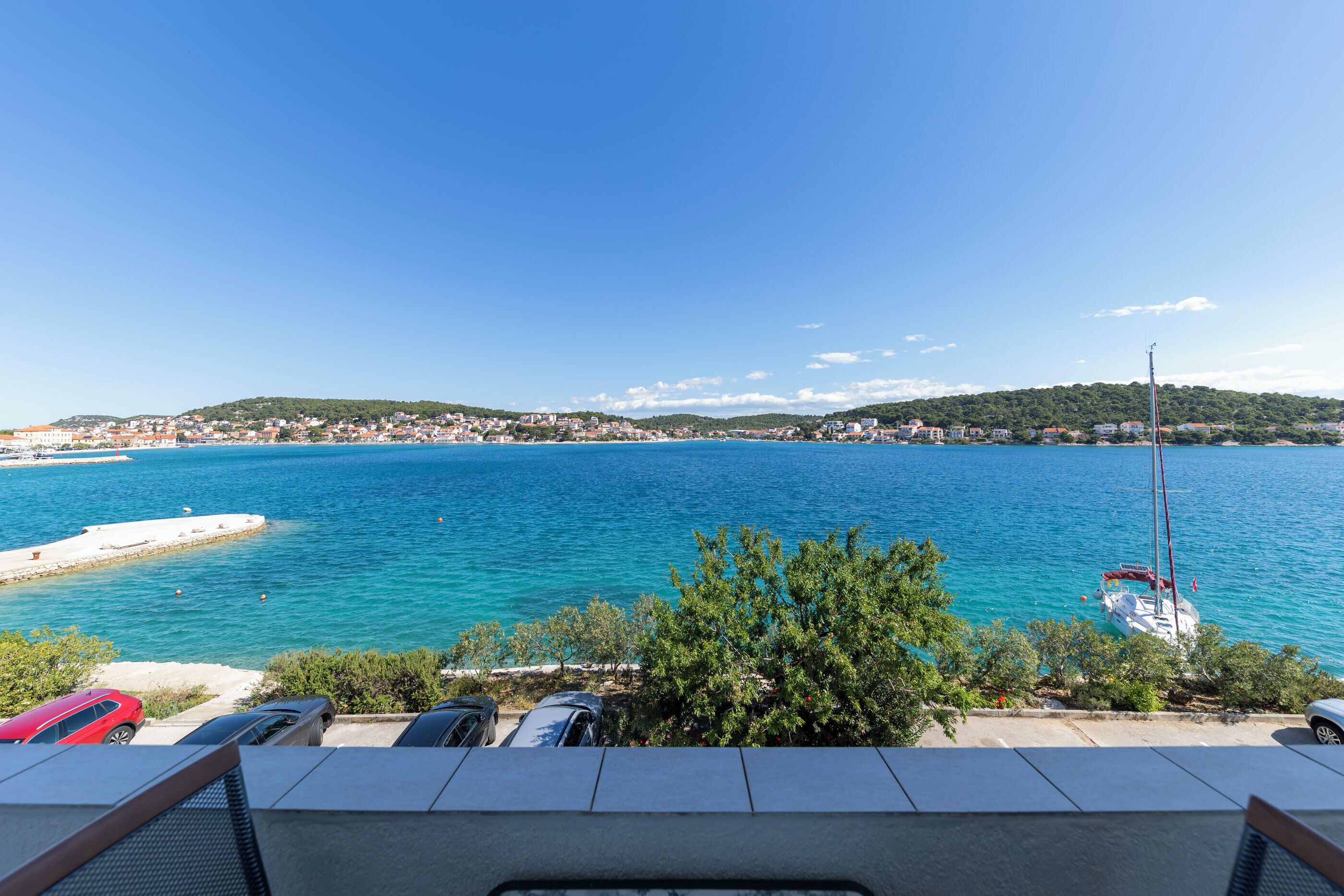 A coastal view with a clear sky, a body of water, and a distant hill with buildings.