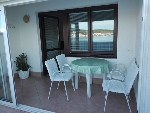 Un balcón con mesa y sillas, una planta en maceta y vistas al mar.