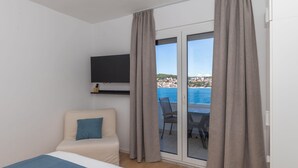 Een slaapkamer met een bed, een aan de muur bevestigde televisie, een stoel en uitzicht op de zee door een schuifdeur.