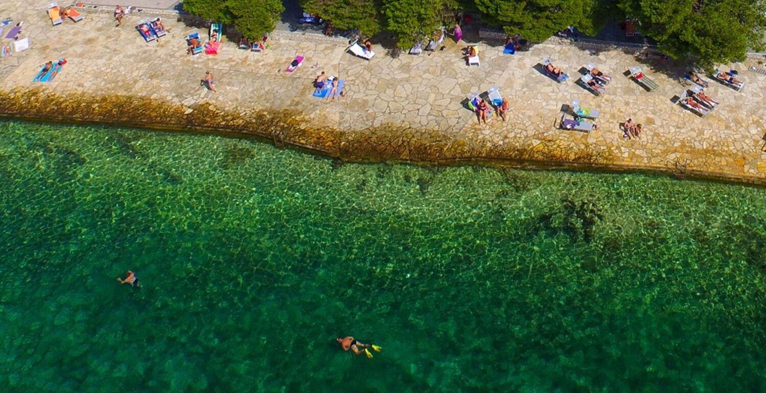 An aerial view of a beach with clear water, people sunbathing, and a few swimmers.