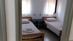 A room with two beds, a small table, and a window with curtains. - Apartments Mari (Nin)