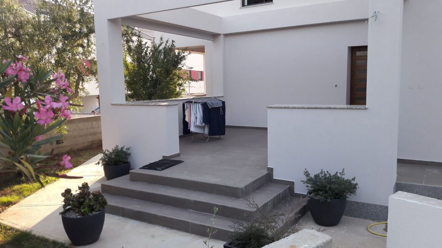 A modern building with a covered entrance, steps leading up to a door, and potted plants around the entrance area.