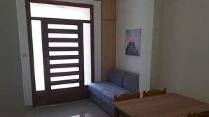 A room with a wooden door, a sofa, a dining table with chairs, and a wall-mounted picture. - Apartments Mari (Nin)