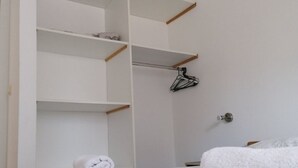 A hotel room with a bed, a wardrobe with multiple shelves, and a hanging garment rack. - Apartments Mari (Nin)