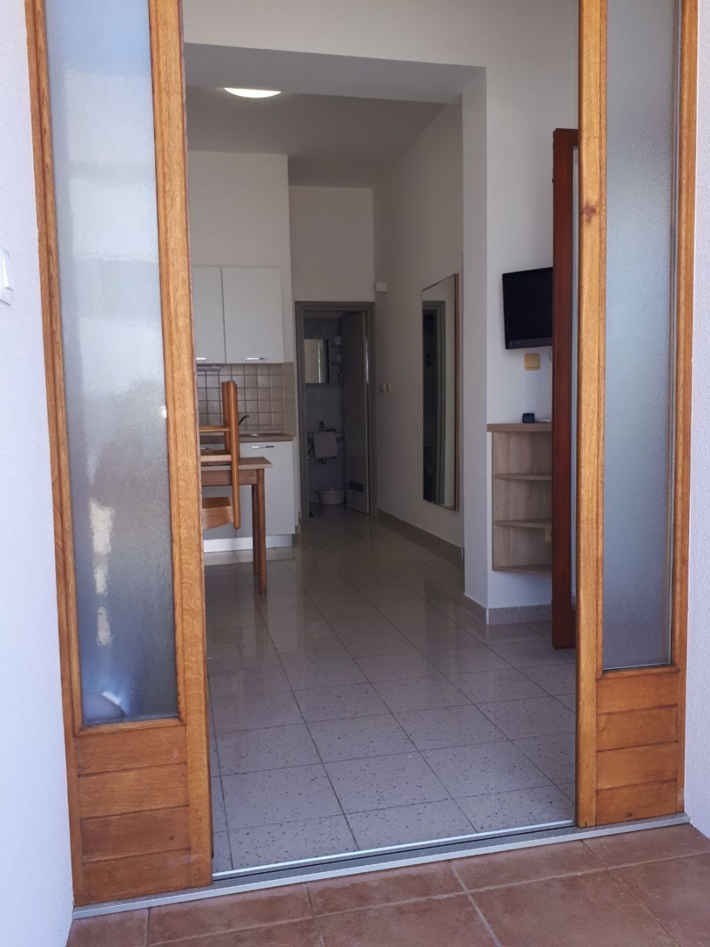 A hallway with a wooden door, a kitchen area, and a bathroom visible through an open door.
