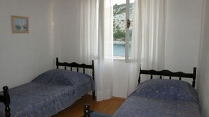 Een kamer met twee bedden, een raam met gordijnen en uitzicht op een kustlandschap.