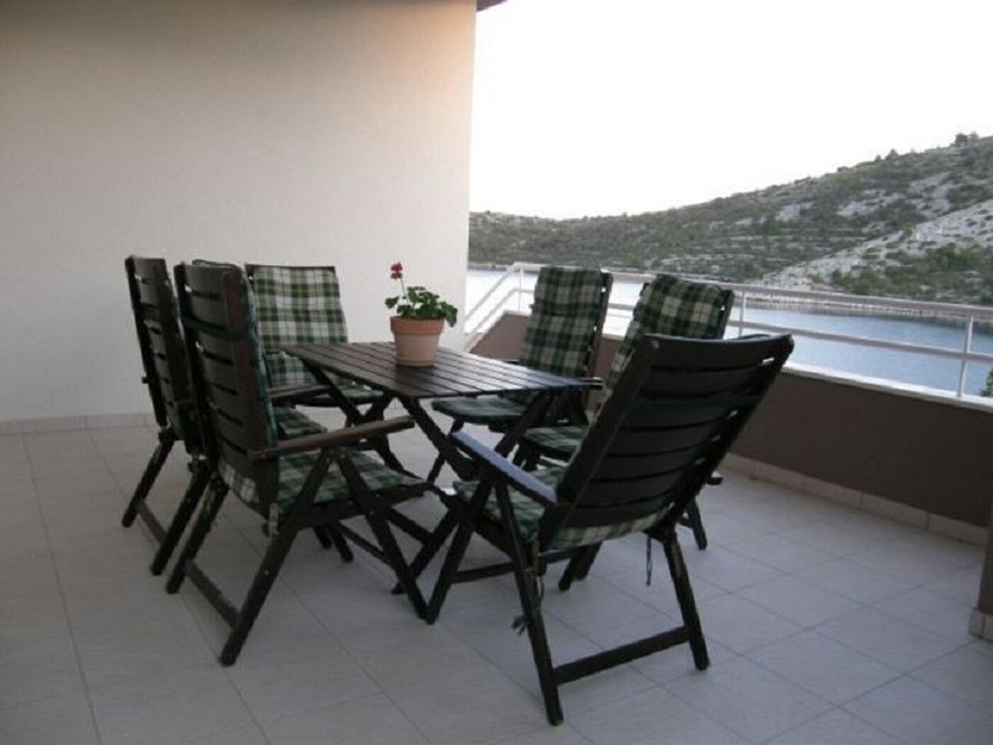 A balcony with a table and chairs, a potted plant, and a view of a hilly landscape.