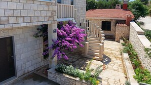Un edificio de piedra con techo de tejas, una escalera que conduce a un balcón y un jardín de flores púrpuras.