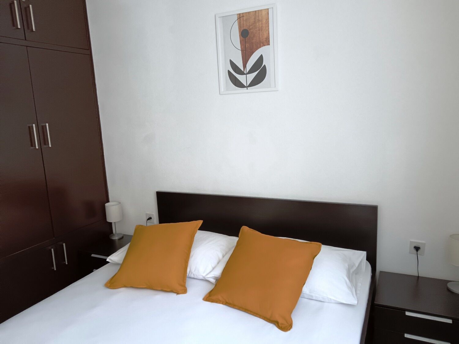 A neatly made bed with two pillows, a dark headboard, and a small bedside table with a lamp.