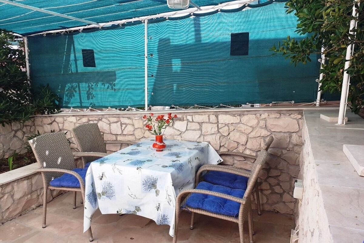 A patio with a table and chairs, a stone wall, and a blue canopy.